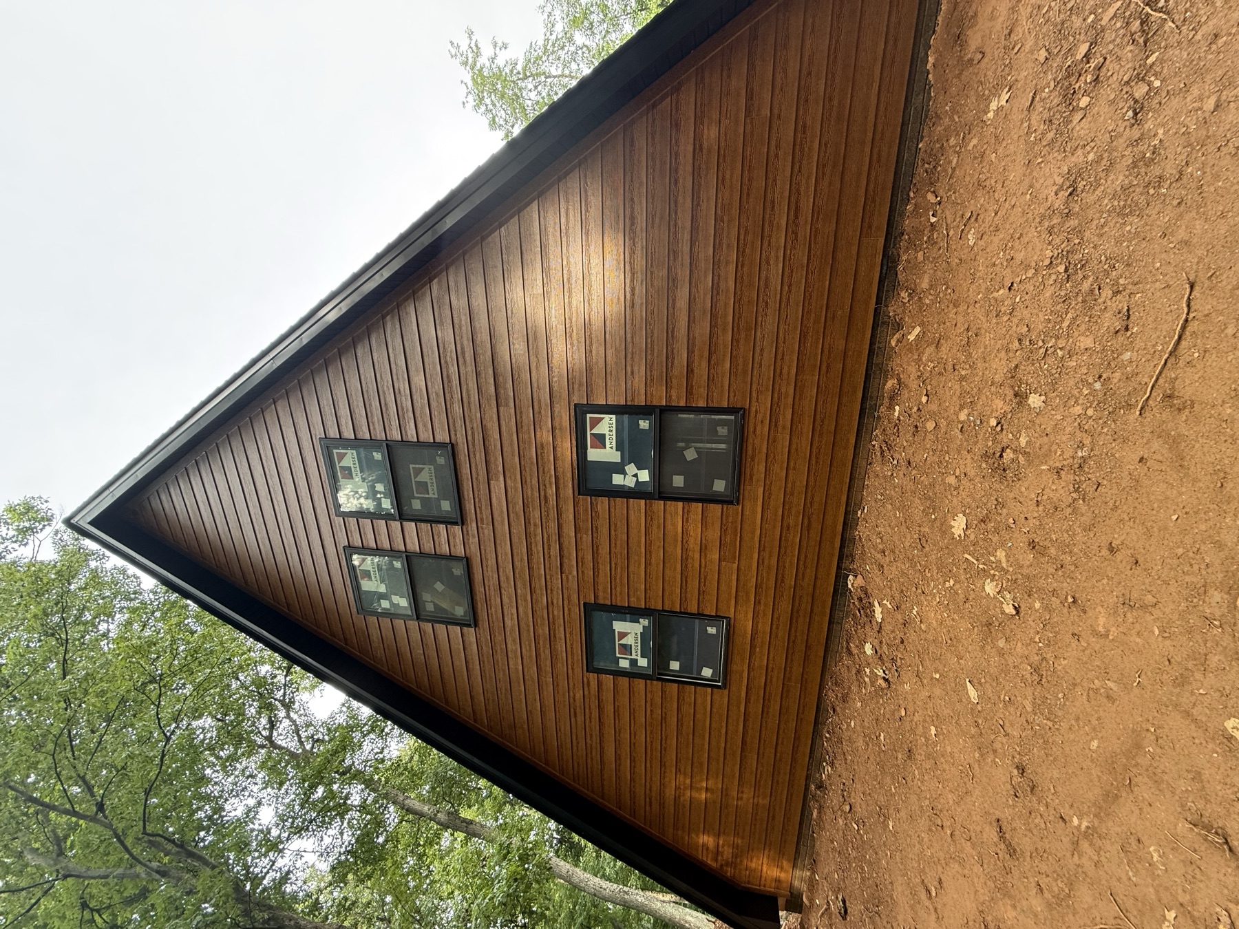 Wood-look siding and black-trimmed windows on a custom A-frame home in the woods